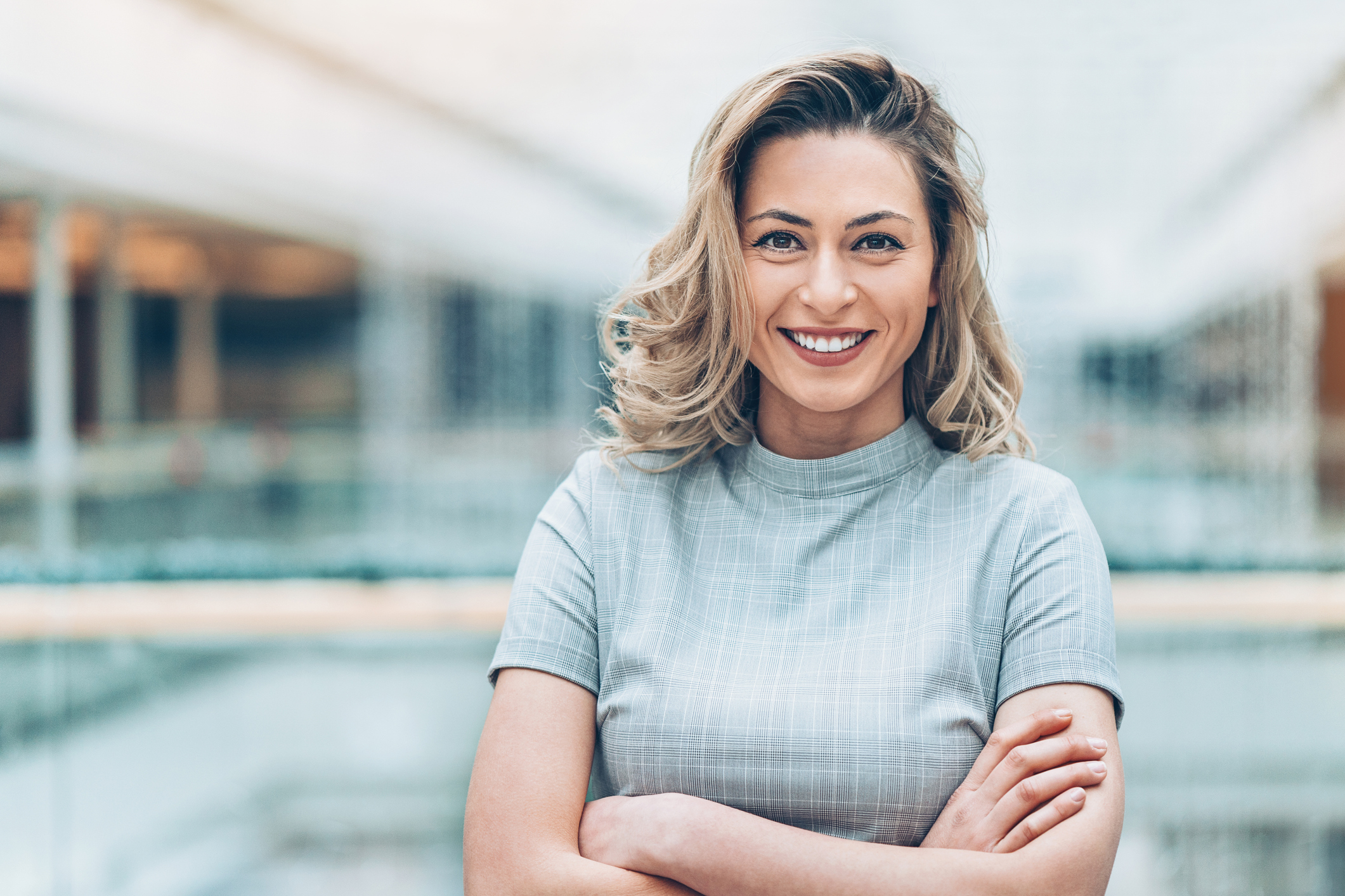 Foto einer selbstbewussten, lächelnden Frau mit verschränkten Armen